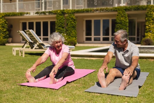Senior caucasian couple practicing yoga, stretching in sunny garden. retirement retreat and active senior lifestyle concept.