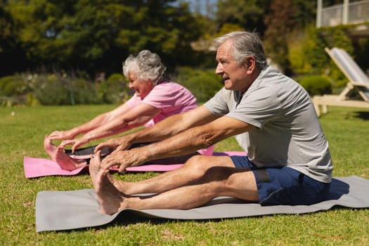 Senior caucasian couple practicing yoga, stretching in sunny garden. retirement retreat and active senior lifestyle concept.