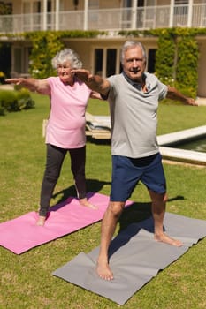 Senior caucasian couple practicing yoga, stretching in sunny garden. retirement retreat and active senior lifestyle concept.