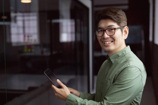 Portrait of smiling asian businessman standing in empty office using tablet. working in business at a modern office.