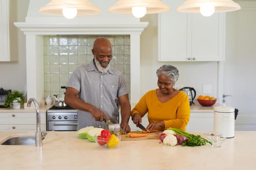 Senior african american couple cooking together in kitchen smiling. retreat, retirement and happy senior lifestyle concept.