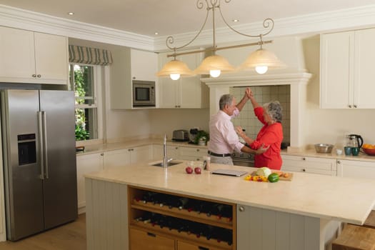 Senior caucasian couple dancing together and smiling in kitchen. retreat, retirement and happy senior lifestyle concept.