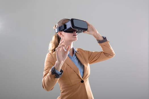 Caucasian businesswoman wearing vr headset touching virtual interface, isolated on grey background. business, technology, communication and growth concept.