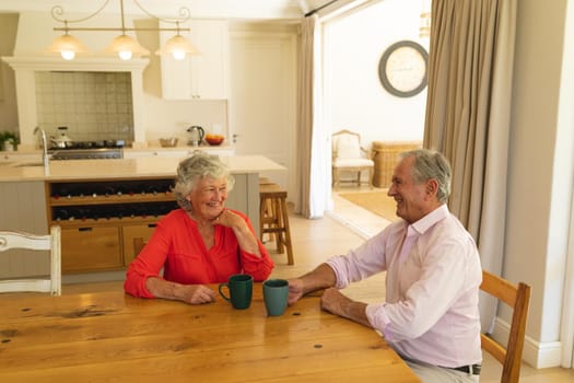 Senior caucasian couple sitting at table together drinking coffee in kitchen. retreat, retirement and happy senior lifestyle concept.