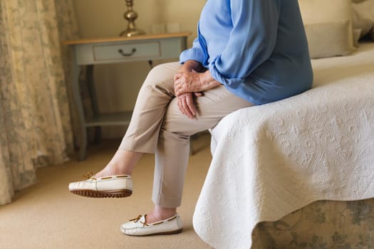 Senior caucasian woman sitting on bed and thinking in bedroom. retreat, retirement and senior lifestyle concept.