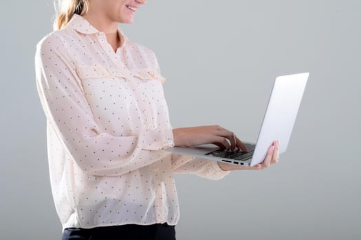 Smiling caucasian businesswoman using laptop, isolated on grey background. business, technology, communication and growth concept.