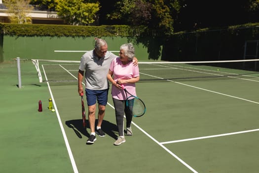 Senior caucasian couple embracing and smiling on tennis court. retirement retreat and active senior lifestyle concept.