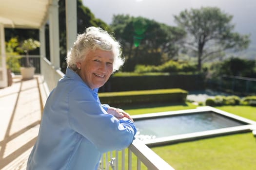 Portrait of senior caucasian woman standing on balcony and smiling. retreat, retirement and happy senior lifestyle concept.