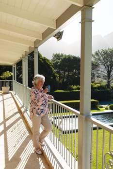 Senior caucasian woman standing on balcony holding mug and smiling. retreat, retirement and happy senior lifestyle concept.