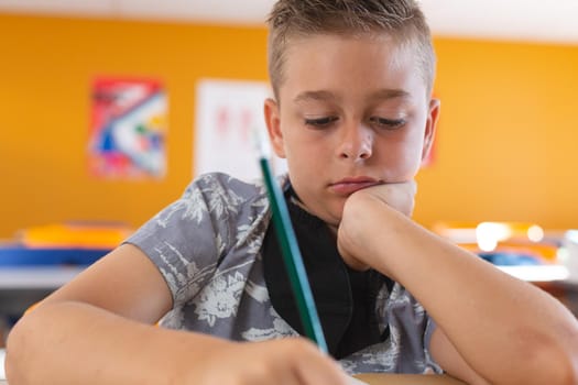 Caucasian schoolboy with face mask sitting in classroom concentrating and writing in schoolbook. childhood and education at elementary school during coronavirus covid19 pandemic.