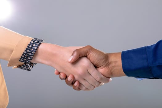 Midsection of caucasian and african american business people shaking hands on grey background. business, technology, communication and growth concept.