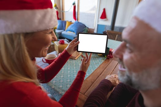 Happy caucasian mature couple making a video call and using tablet with copy space. christmas, festivity and communication technology.
