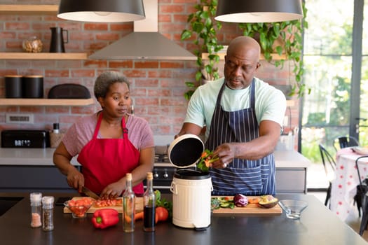 Serious african american senior couple cooking together in kitchen using compost bin. retirement lifestyle, leisure and spending time at home.