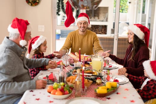 Caucasian multi generation family wearing santa hats praying at christmas table. family christmas time and festivity together at home.