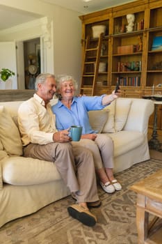 Senior caucasian couple sitting on sofa having video call using smartphone. retreat, retirement and happy senior lifestyle concept.