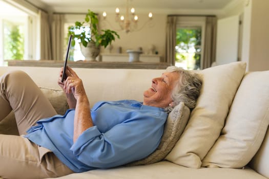 Senior caucasian woman lying on sofa using tablet. retreat, retirement and happy senior lifestyle concept.