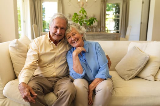 Portrait of senior caucasian couple sitting on sofa embracing and smiling. retreat, retirement and happy senior lifestyle concept.