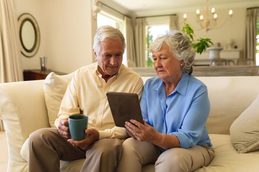 Senior caucasian couple sitting on sofa using tablet. retreat, retirement and happy senior lifestyle concept.