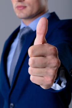 Midsection of caucasian businessman with thumb up, isolated on grey background. business technology, communication and growth concept.