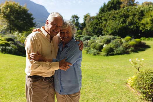 Portrait of senior caucasian couple embracing and smiling in sunny garden. retreat, retirement and happy senior lifestyle concept.