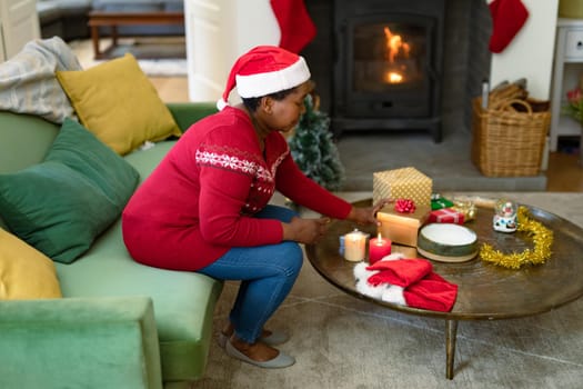 African american senior woman in santa hat opening present at christmas time. retirement lifestyle and christmas festivities, celebrating at home.