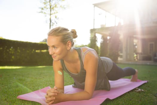 Smiling caucasian woman exercising in sunny garden, doing plank. health, fitness and wellbeing, spending quality time at home.