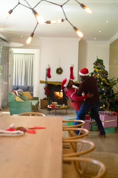 Happy african american senior couple in santa hats dancing at home at christmas time. retirement lifestyle and christmas festivities, celebrating at home.