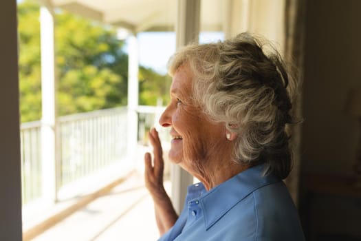 Senior caucasian woman looking through window and smiling. retreat, retirement and happy senior lifestyle concept.