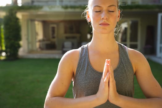 Tranquil caucasian woman practicing yoga in sunny garden, meditating with eyes closed. health, fitness and wellbeing, spending quality time at home.