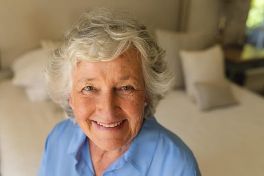 Portrait of senior caucasian woman sitting on bed and smiling in bedroom. retreat, retirement and happy senior lifestyle concept.
