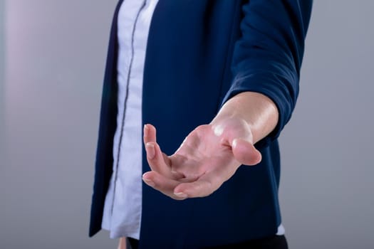 Midsection of caucasian businesswoman reaching with her hand, isolated on grey background. business technology, communication and growth concept digitally generated composite image.