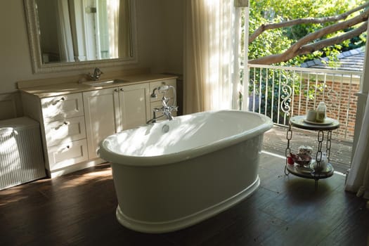 General view of luxury sunny bathroom with bathtub in the middle. interior design and home decoration concept.