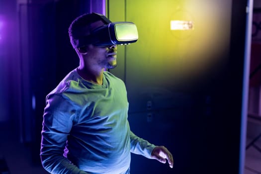 African american male computer technician wearing vr headset and working in server room. digital information storage and communication network technology.