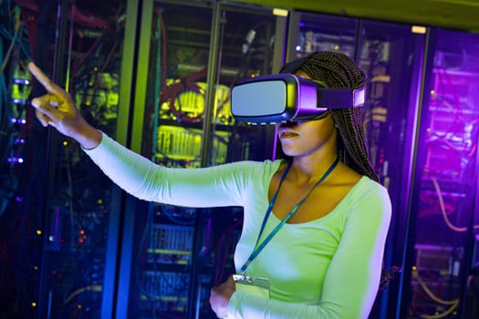 African american female computer technician wearing vr headset and working in server room. digital information storage and communication network technology.