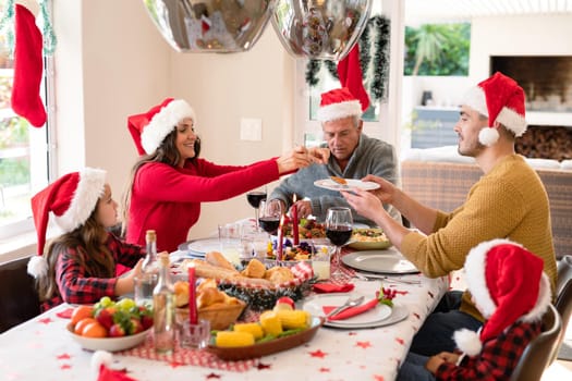 Caucasian multi generation family wearing santa hats having christmas meal. family christmas time and festivity together at home.