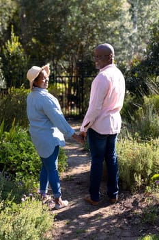 Happy african american senior couple holding hands outdoors. retirement lifestyle, spending time at home and garden.