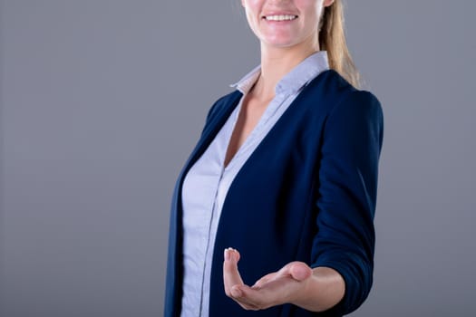 Smiling caucasian businesswoman reaching with her hand, isolated on grey background. business technology, communication and growth concept digitally generated composite image.