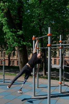 athletic young man with artificial leg working out on a bars. Outdoors