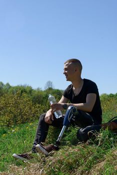 a man on a prosthetic leg travels the mountains. Dressed in black jeans and a T-shirt. sitting on a stone