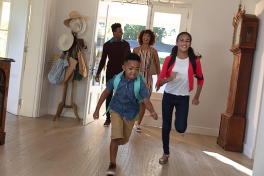 Happy african american couple with son and daughter back from school embracing and smiling at home. family enjoying quality free time together.