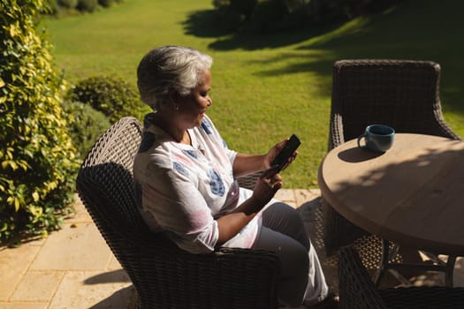 Senior african american woman using smartphone in sunny garden. retreat, retirement and happy senior lifestyle concept.