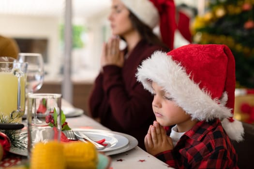 Caucasian boy and his mother praying together at christmas table. family christmas time and festivity together at home.