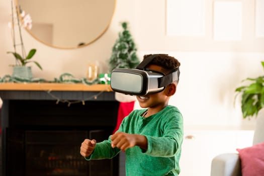 African american boy wearing vr headset and having fun at christmas time. childhood, leisure and discovery using technology at home.