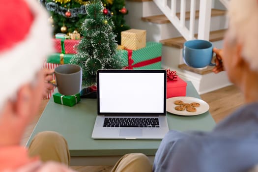 Back view of caucasian senior couple using laptop, having video call at christmas time. christmas, festivity and communication technology.