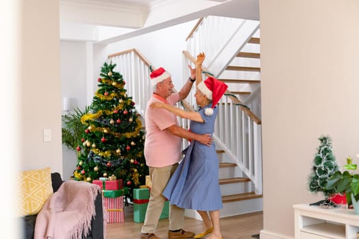 Happy caucasian senior couple wearing santa hat dancing at christmas time. christmas, festivity and tradition at home.