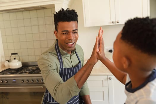 Happy african american father and son high fiving in kitchen before cooking. family enjoying quality free time together.