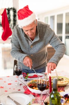 Happy caucasian senior man cutting food at christmas table. family christmas time and festivity together at home.