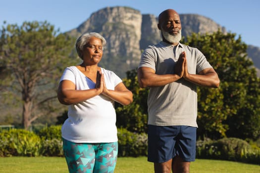 Senior african american couple meditating and practicing yoga with eyes closed in countryside. retirement and active senior lifestyle concept.