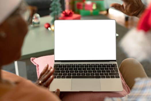 Back view of african american couple using laptop with copy space at christmas time. christmas, festivity and communication technology at home.