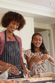 Happy african american mother with daughter baking in kitchen, cutting cookies. family enjoying quality free time together.